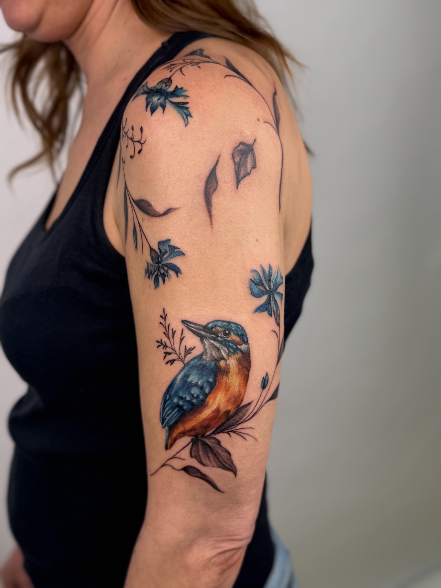 Farbiges Tattoo eines blau-orangefarbenen Eisvogels mit Blüten und Zweigen am Arm