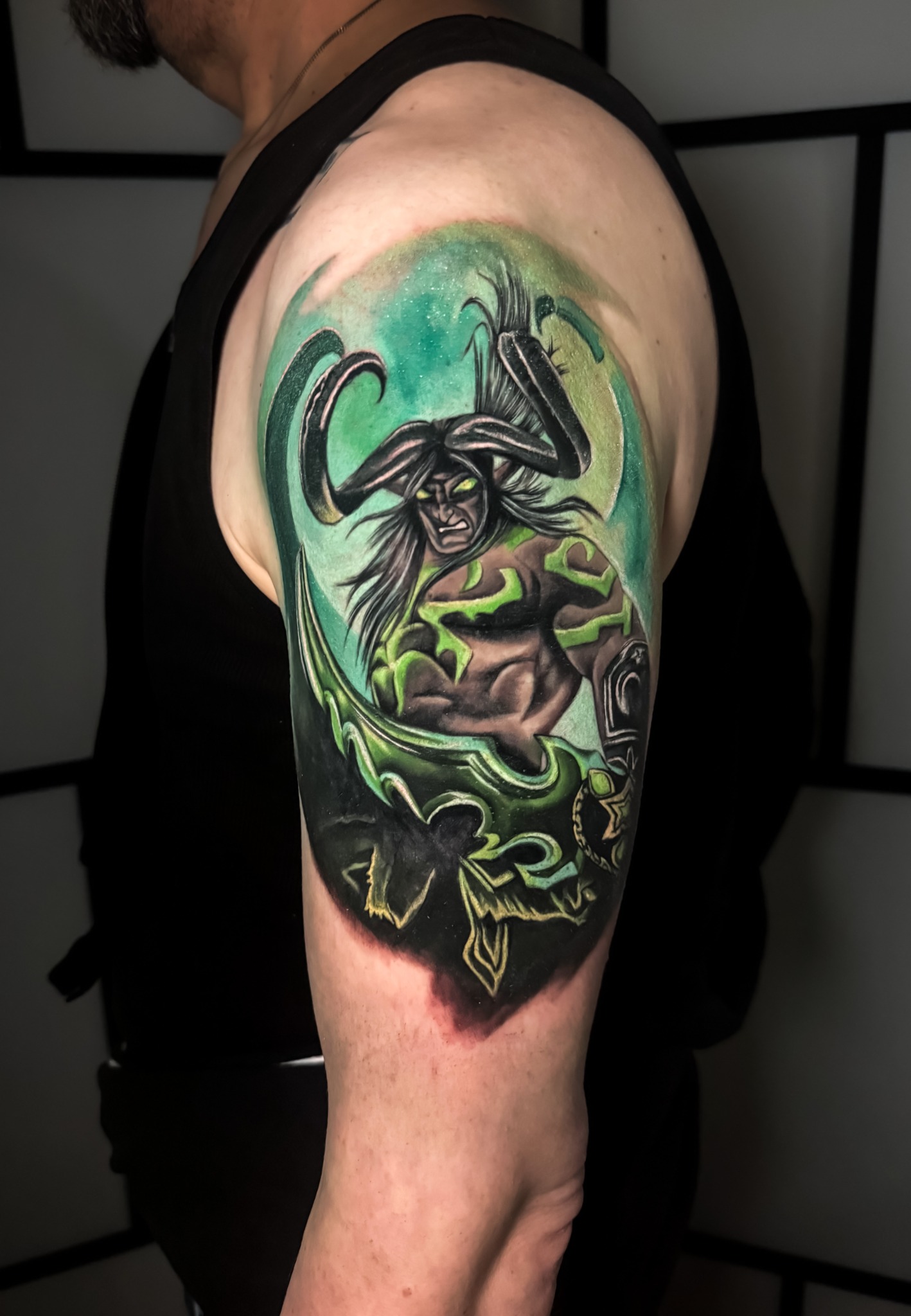 Grünes Fantasiewesen mit Hörnern, Blättern und türkisfarbenem Hintergrund als Tattoo am Oberarm