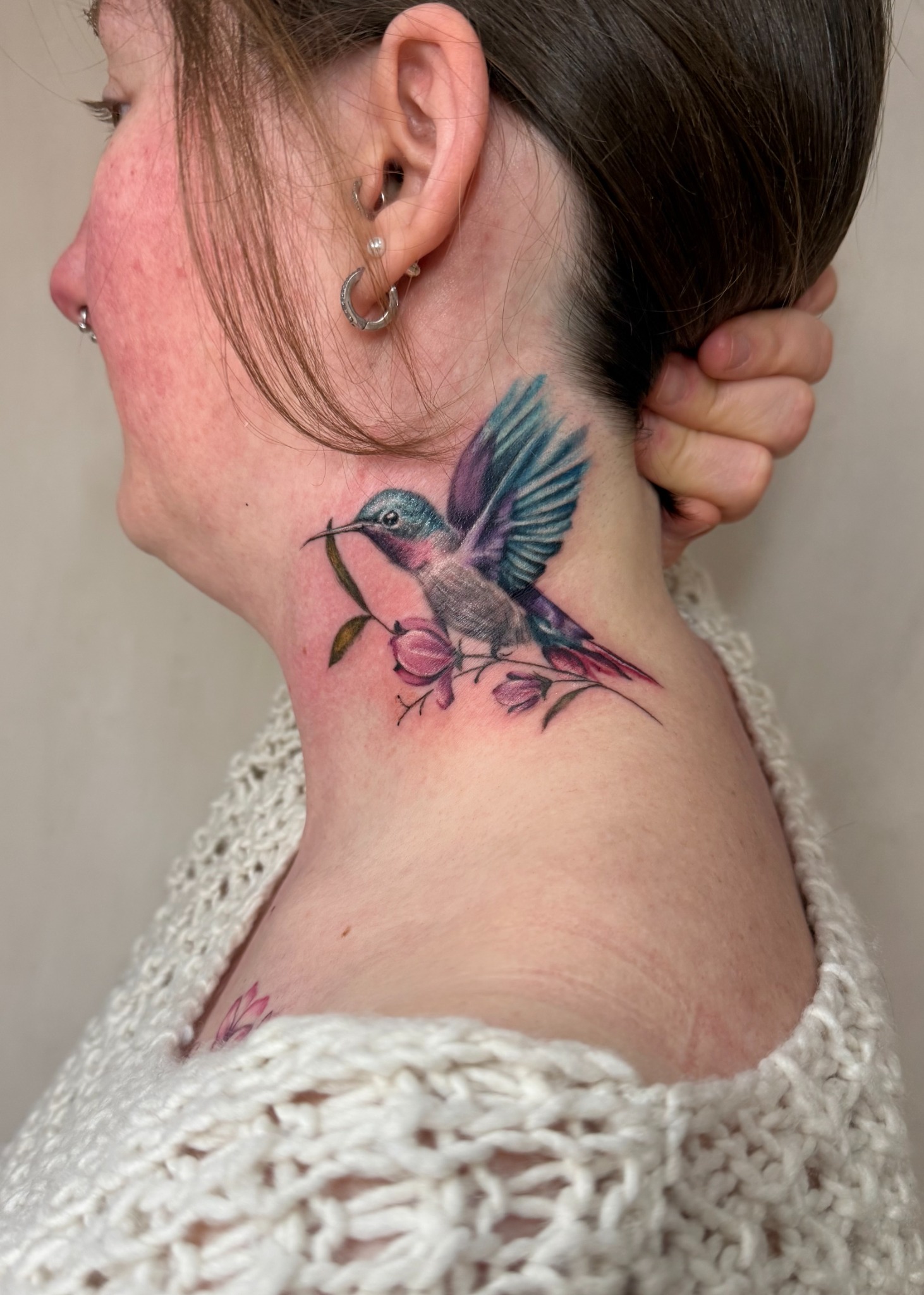 Blau-grüner Kolibri mit rosafarbenen Blüten als Tattoo seitlich am Hals