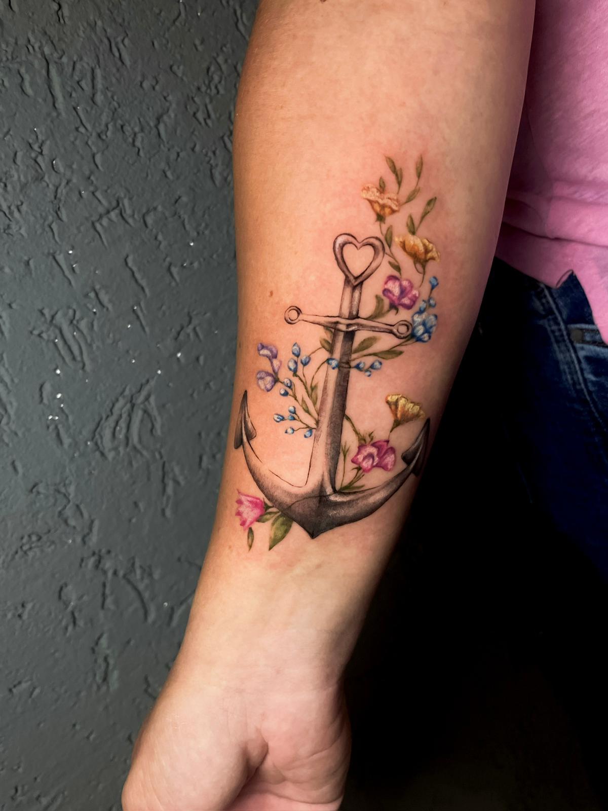 Anker-Tattoo am Unterarm mit Herzdetail und kleinen farbigen Blumen