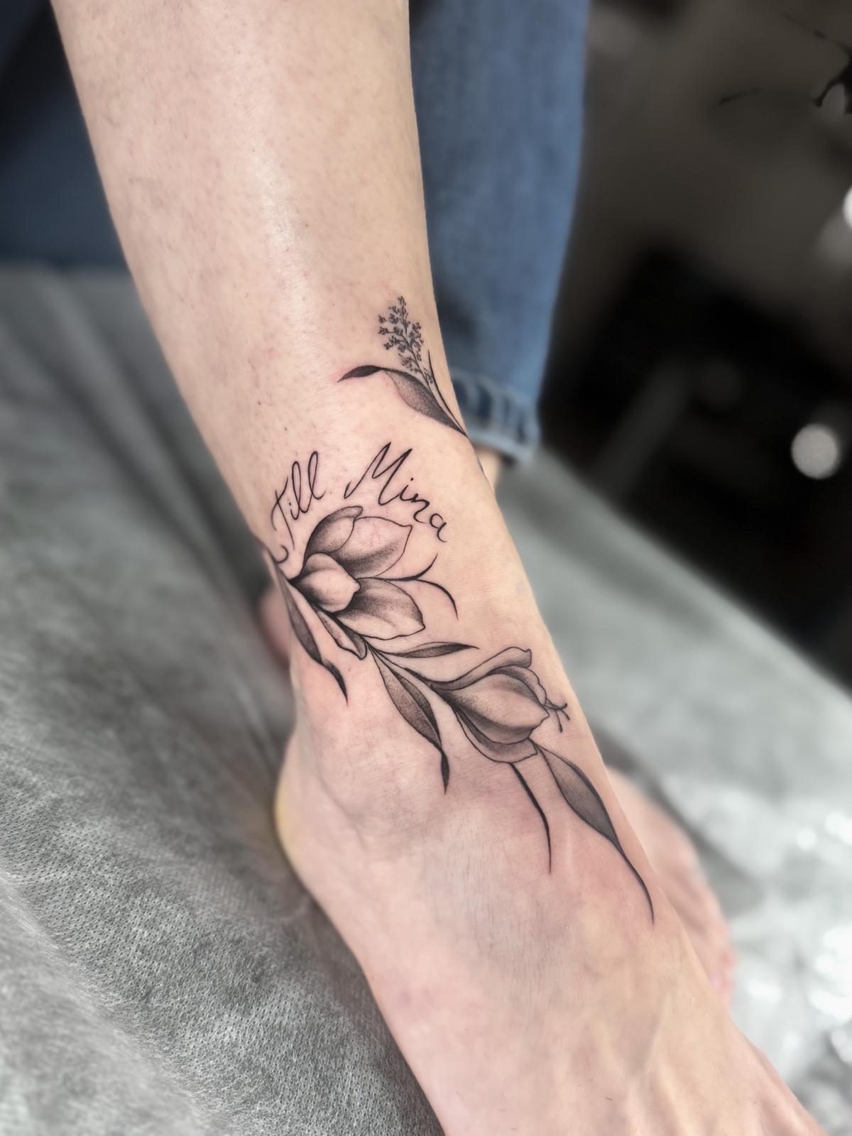 Filigrane Blume mit Blättern und einem Schriftzug am Handgelenk