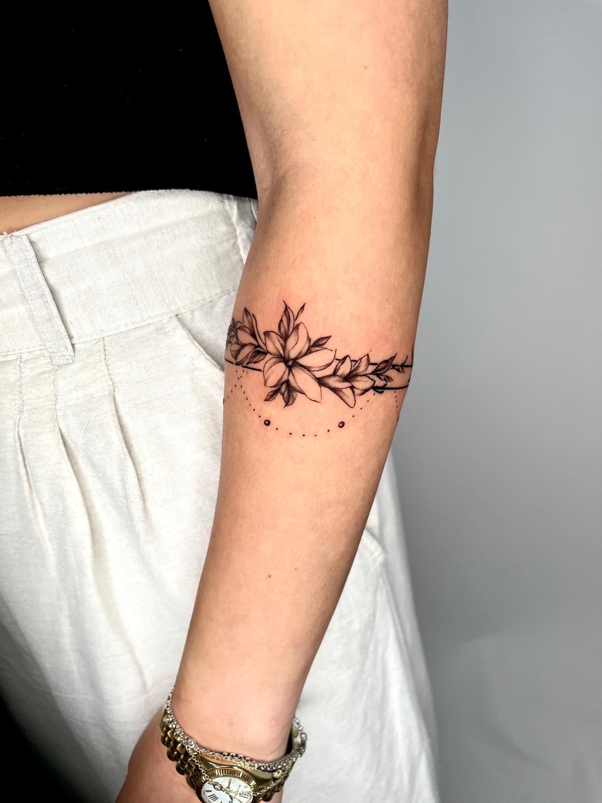 Florales Tattoo-Armband mit feinen Blüten und Blättern um den Unterarm