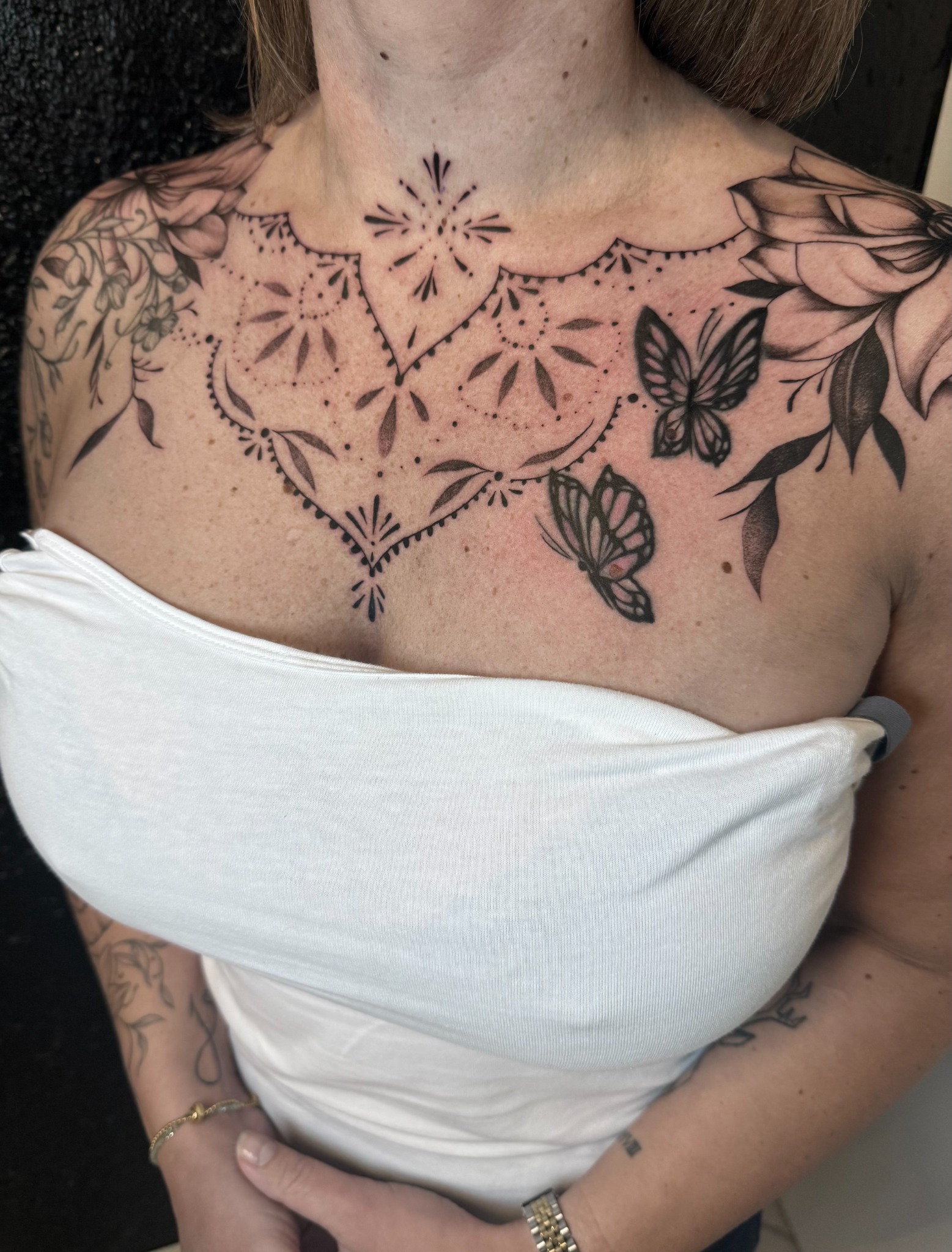 Symmetrisches Ornamental Tattoo am Dekolleté mit floralen Elementen und Schmetterlingen
