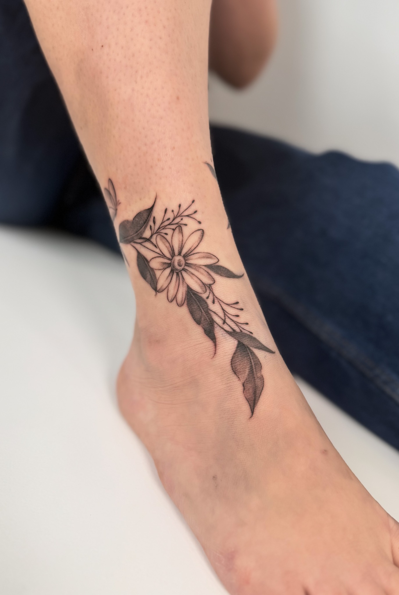 Filigranes schwarzes Blumen-Tattoo mit Blättern am Handgelenk