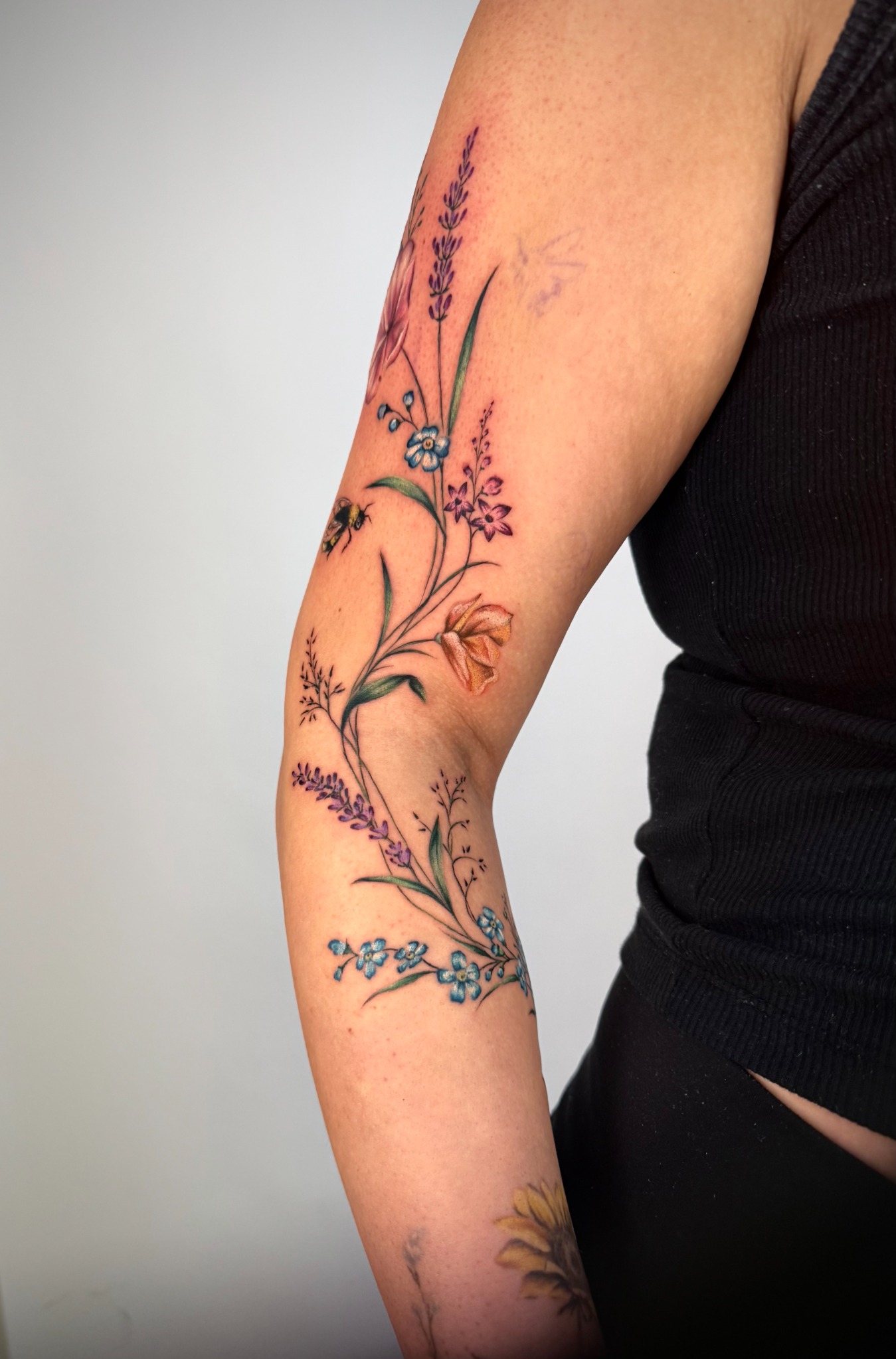 Filigranes farbiges Blumen-Tattoo am Arm mit violetten Blüten und grünen Blättern
