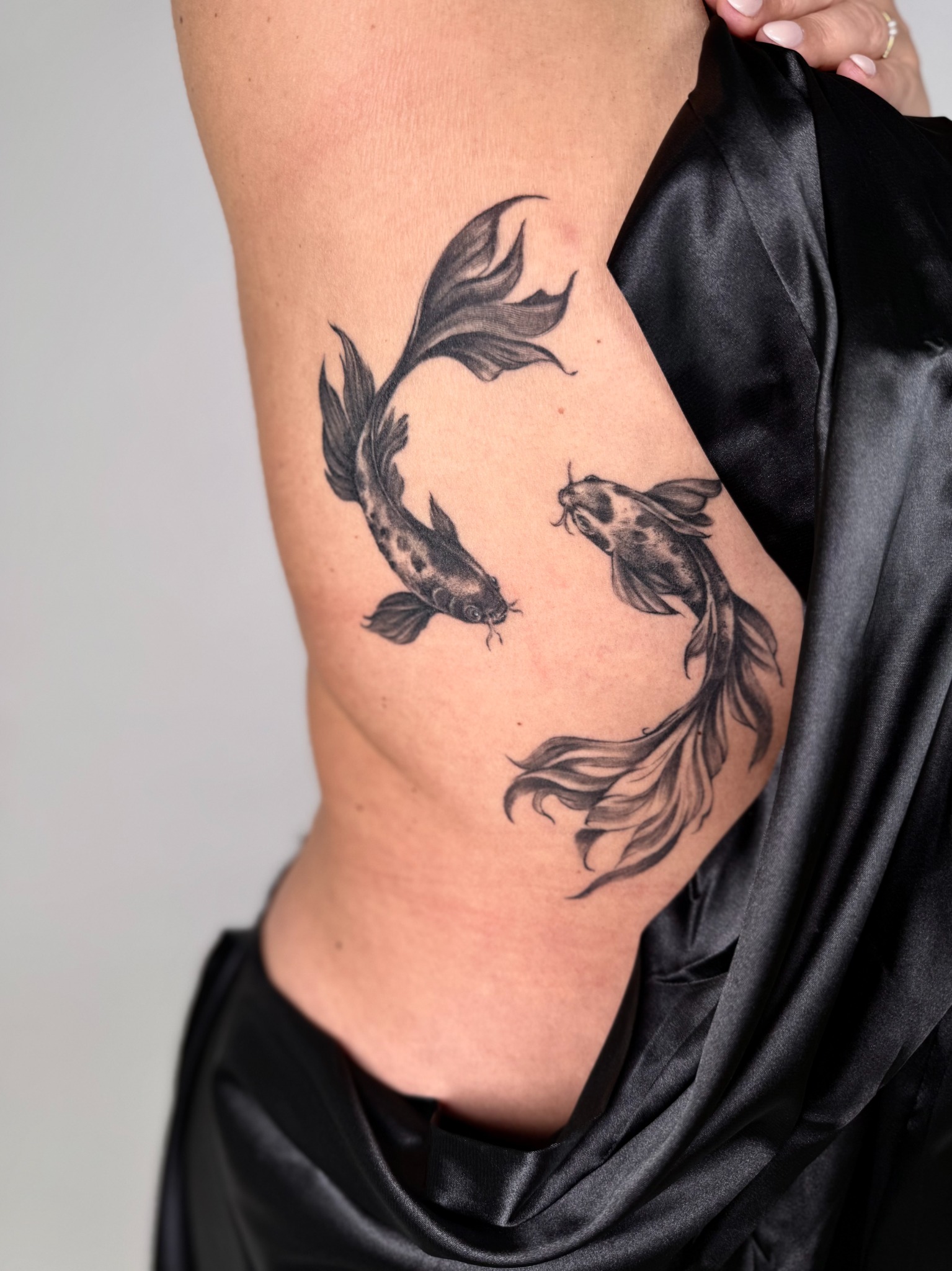 Zwei Fische mit geschwungenen Flossen als schwarzes Tattoo an der seitlichen Rippenpartie