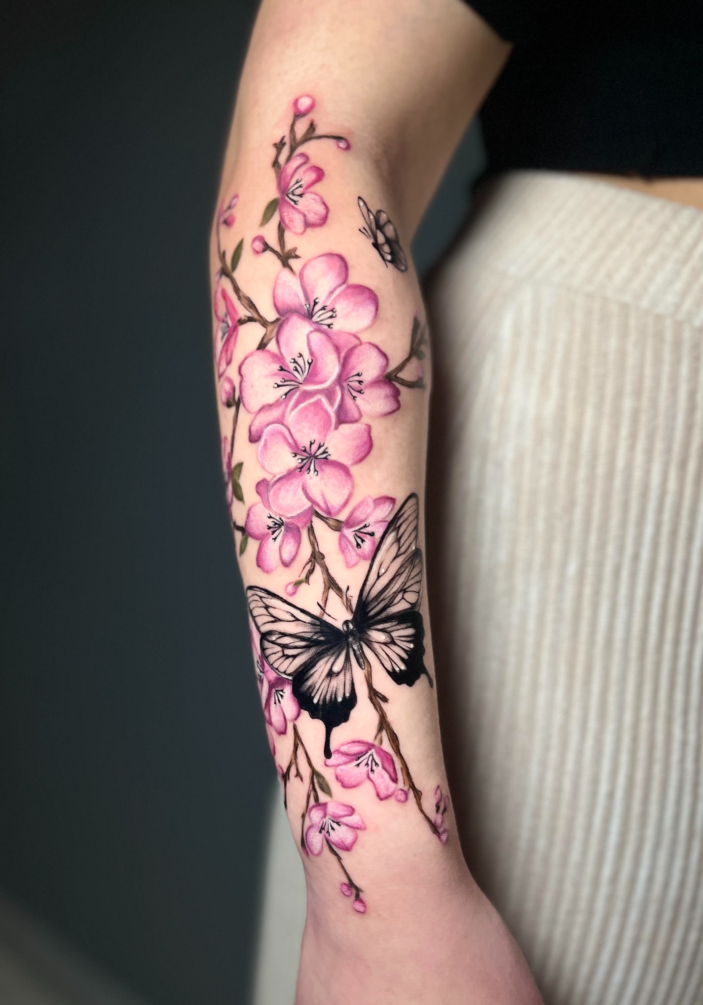 Rosa Orchideen mit einem schwarz schattierten Schmetterling als Tattoo am Unterarm
