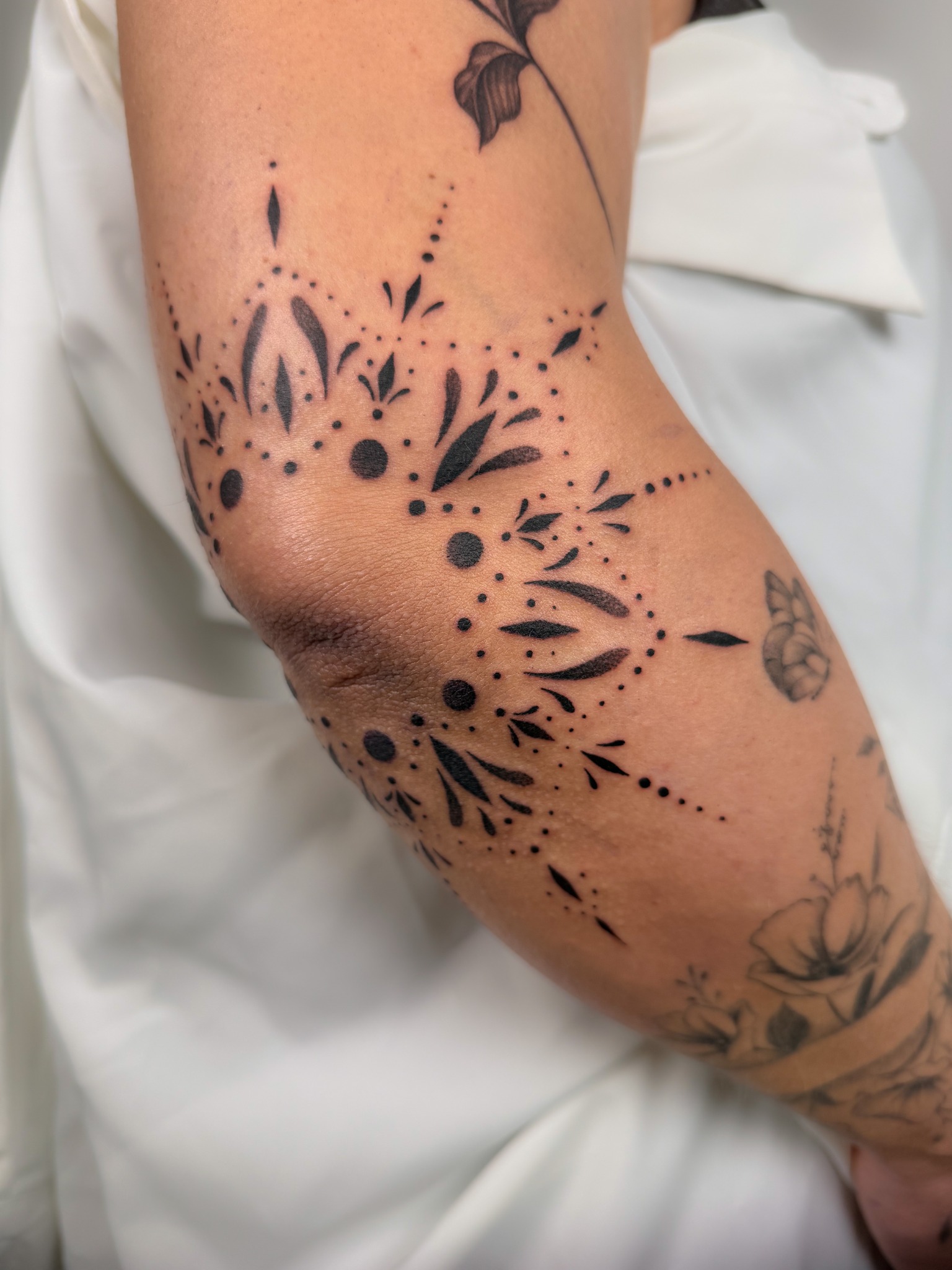 Ornamental Tattoo um den Ellenbogen mit blattförmigen Elementen und Punktlinien