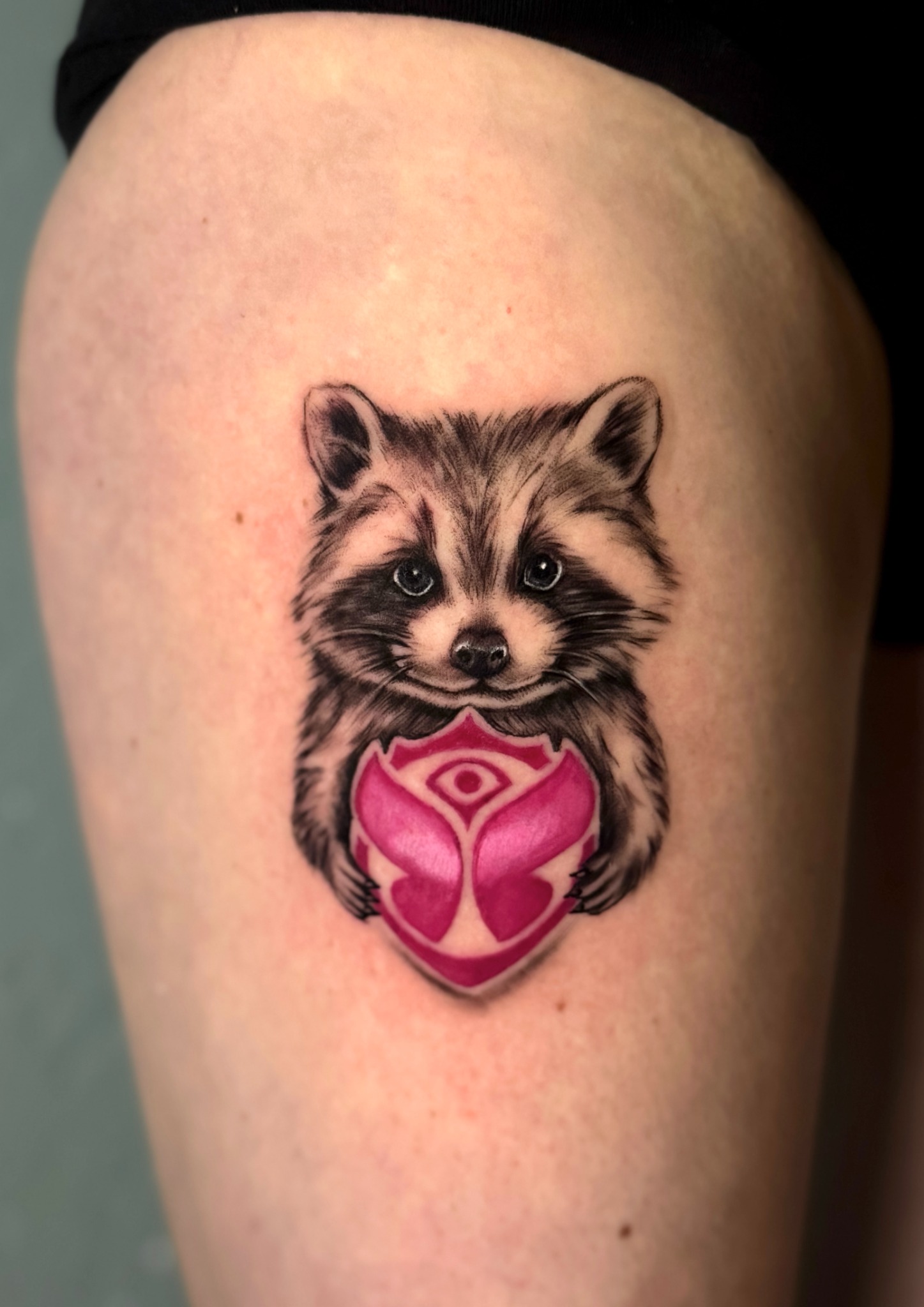 Waschbär-Tattoo mit einem pinken Herzmotiv am Oberarm